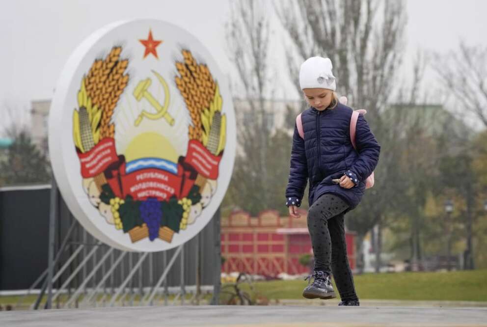 A girl walks past an emblem of the Transnistrian Moldavian Republic in Tiraspol, the capital of the breakaway region of Transnistria, a disputed territory unrecognized by the international community, in Moldova, Monday, Nov. 1, 2021. (AP Photo/Dmitri Lovetsky)
