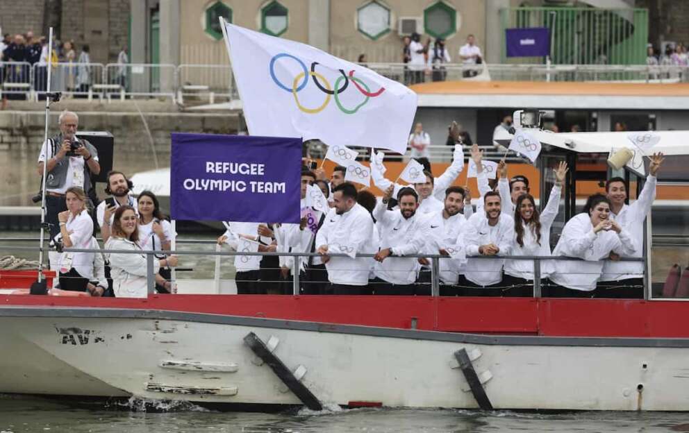 Athletes of the Refugee Olympic Team wave aboard a boat in the floating parade on the Seine River in Paris, France, during the opening ceremony for the 2024 Summer Olympics, Friday, July 26, 2024. (Nir Elias/Pool Photo via AP)