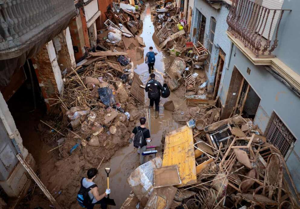 People walk through a street with piled furniture and rubbish on the sides in an area, affected by floods, in Paiporta, Valencia, Spain, Tuesday, Nov. 5, 2024. (AP Photo/Emilio Morenatti)