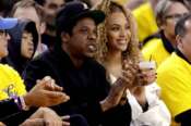 FILE – In this April 28, 2018, file photo, Jay-Z and Beyonce watch Game 1 of an NBA basketball second-round playoff series between the Golden State Warriors and the New Orleans Pelicans in Oakland, Calif. Just as a movie soundtrack helps viewers follow the action of the narrative through each plot twist, hip-hop has done the same for basketball via the NBA. It underscores how hip-hop has used the NBA to step outside its urban origins and reach every corner of the country. Once derided by mainstream America, the words and contributions of hip-hop artists now impact the masses. Jay-Z not only bought a minority a stake in the Brooklyn Nets but designed the uniforms. (AP Photo/Marcio Jose Sanchez, File)